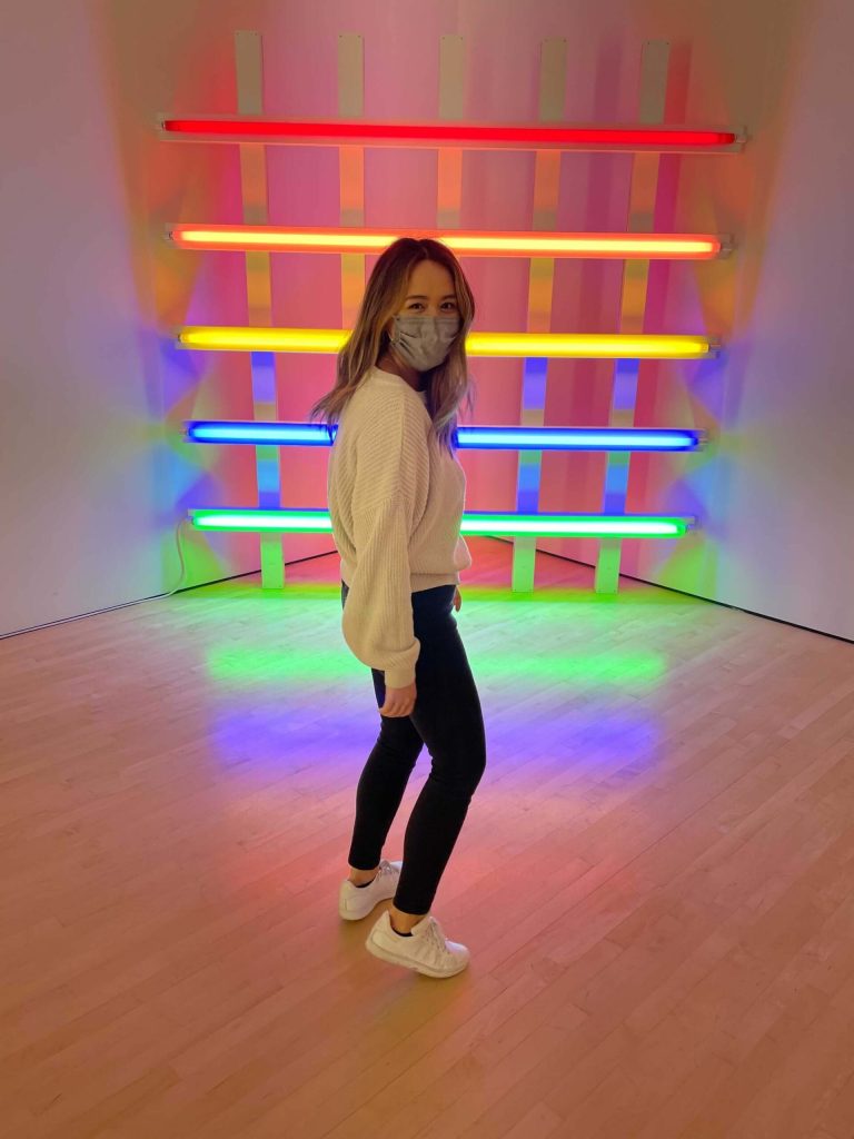 Leilani Click standing in front of rainbow neon lights