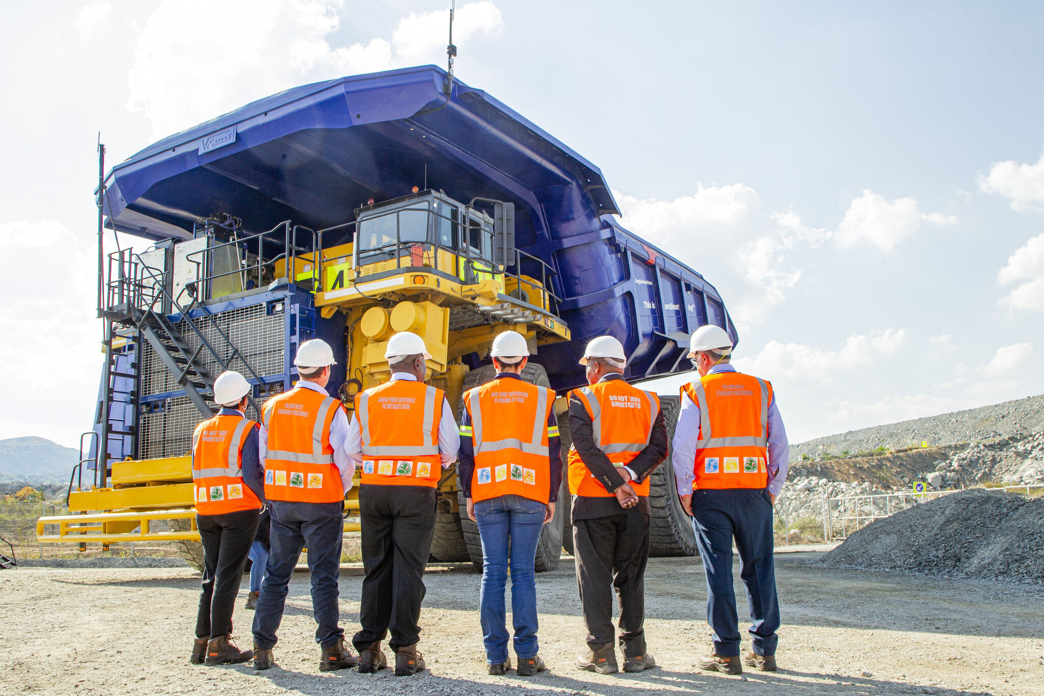 A group of people in PPE standing in front of an ultra-class mining haul truck.