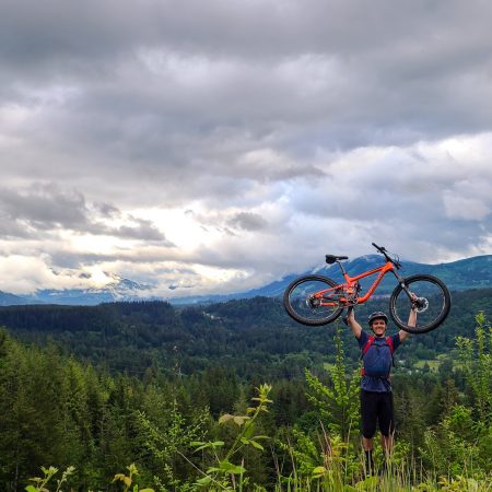 Tyler Weir on a mountainside holding a bike over his head.