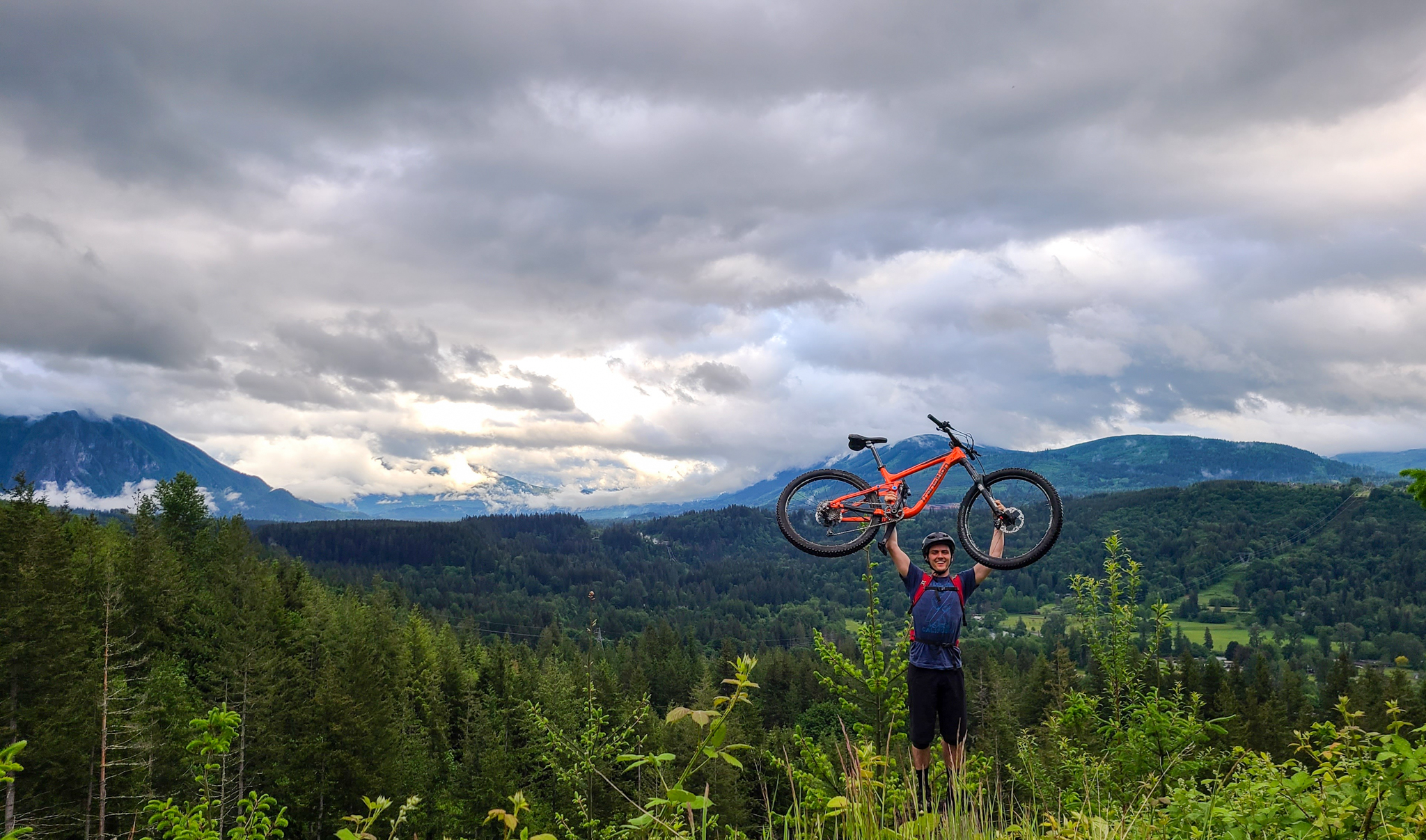 Tyler Weir on a mountainside holding a bike over his head.