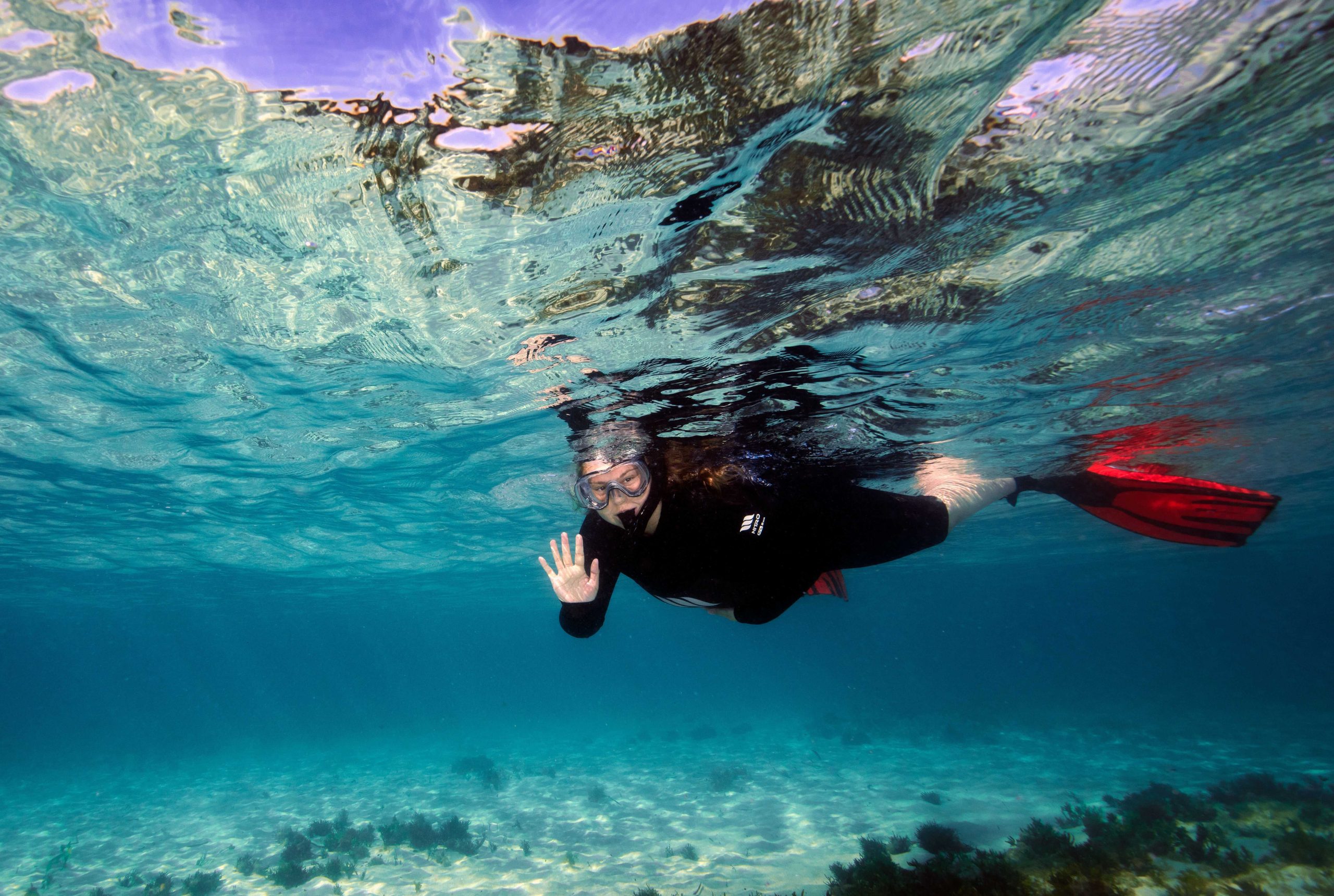 Amber Baurley snorkeling underwater, waving to the camera